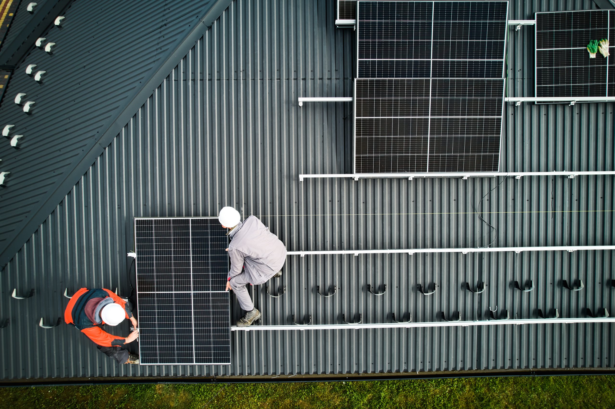 Mounters building photovoltaic solar module station on roof of house. Men electricians in helmets installing solar panel system outdoors. Concept of alternative and renewable energy. Aerial view.