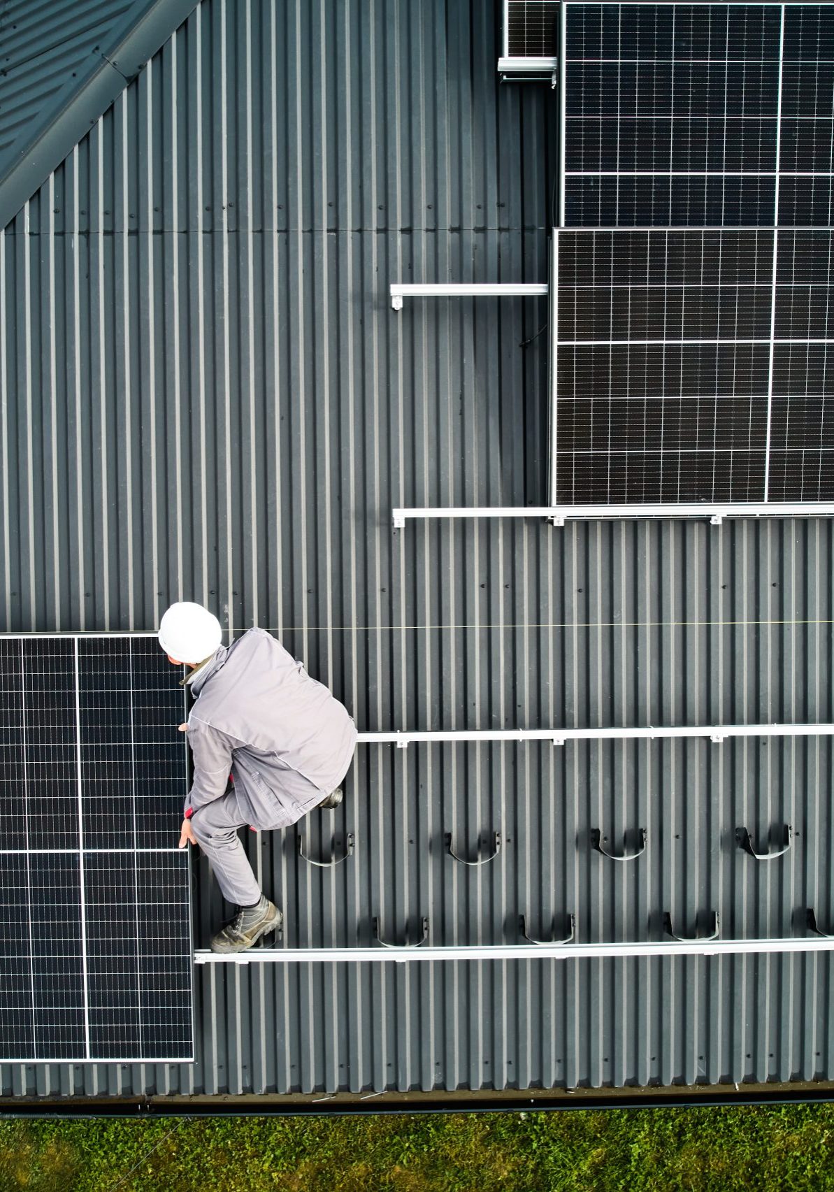 Mounters building photovoltaic solar module station on roof of house. Men electricians in helmets installing solar panel system outdoors. Concept of alternative and renewable energy. Aerial view.